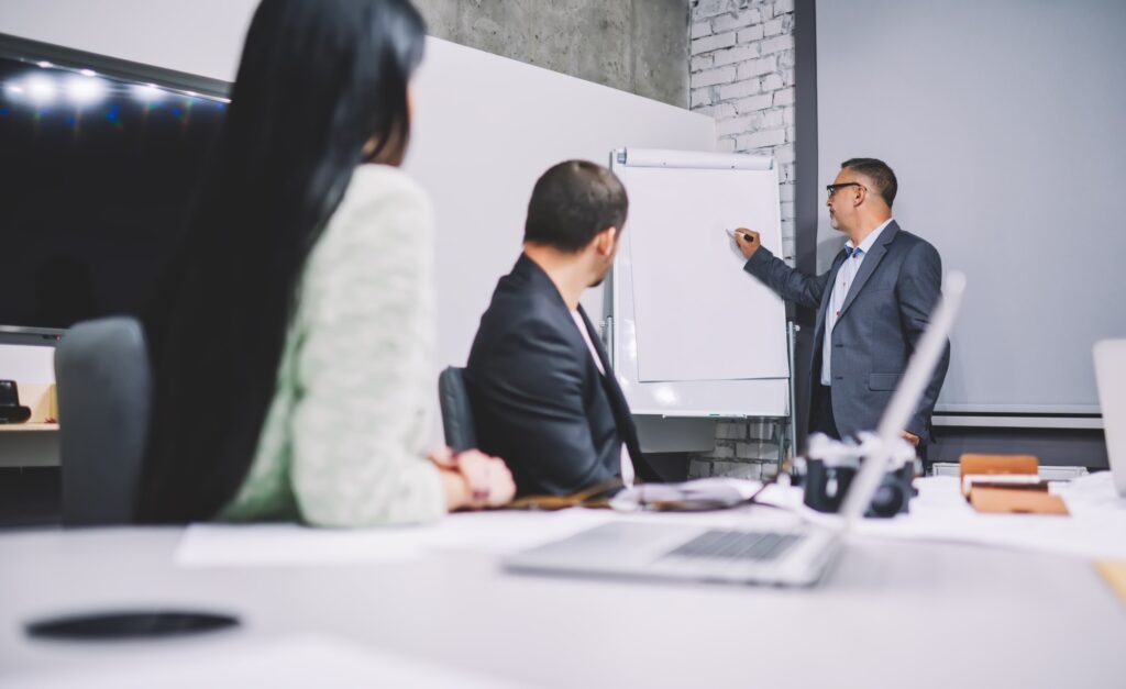 Mature corporate director in formal suit teaching colleagues explaining business strategy near fli